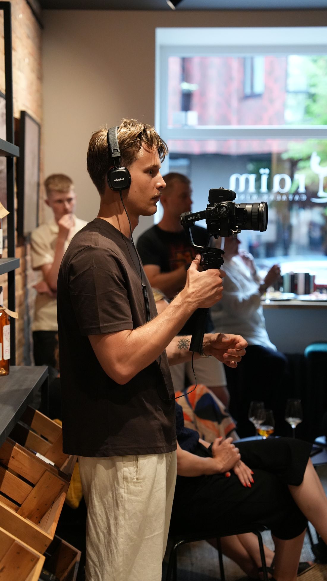 Rudolfs filming with a gimbal-mounted camera during an event in a café